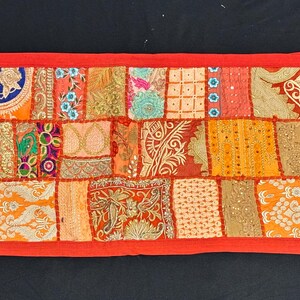 May include: A rectangular, patchwork textile with a vibrant mix of colors including orange, red, and gold. The design features various patterns and textures, framed by a solid red border. This decorative piece is suitable for home decor.