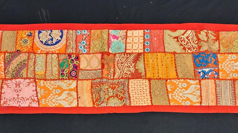 May include: A rectangular, patchwork textile with a vibrant mix of colors including orange, red, and gold. The design features various patterns and textures, framed by a solid red border. This decorative piece is suitable for home decor.