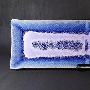 May include: Rectangular ceramic serving dish with a textured blue border and a lavender center. The dish has a speckled pattern and a glossy finish. The design is a modern take on a classic serving piece.