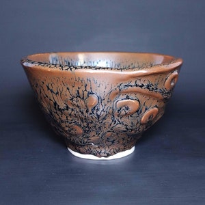 May include: A brown ceramic bowl with a black and white marbled glaze. The bowl has a rounded shape and a slightly flared rim.