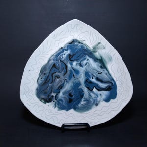 May include: A white triangular ceramic plate with a blue, black, and white marbled design in the center. The plate has a white, wavy, embossed pattern around the edge.