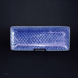 May include: A rectangular blue ceramic serving tray with a textured surface. The tray has a light blue glaze with a subtle purple hue.