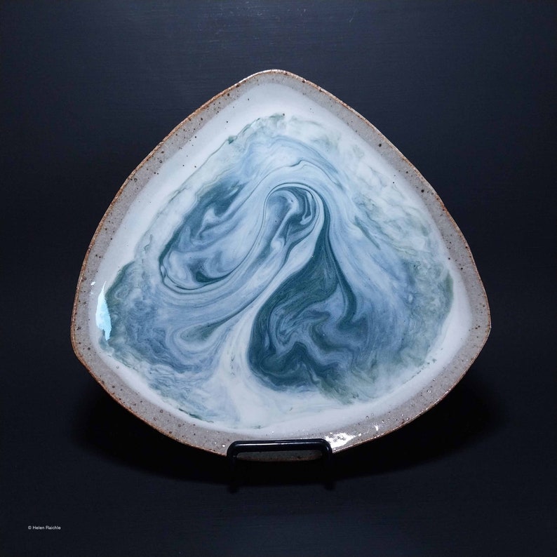 K&ouml;nnte beinhalten: Ein dreieckiger Keramikteller mit wei&szlig;er Glasur und einem wirbelnden, marmorierten Design in Blau und Gr&uuml;n.