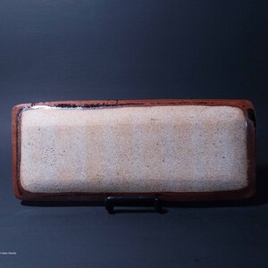 Puede incluir: Una bandeja rectangular de cer&aacute;mica con un borde marr&oacute;n y un interior blanco. La bandeja tiene un esmalte moteado y la firma "Helen Rauch" es visible en la parte inferior.