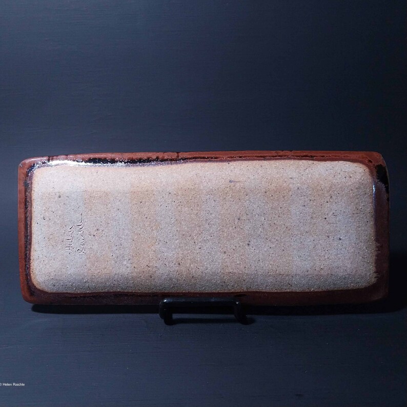 Puede incluir: Una bandeja rectangular de cer&aacute;mica con un borde marr&oacute;n y un interior blanco. La bandeja tiene un esmalte moteado y la firma "Helen Rauch" es visible en la parte inferior.
