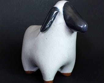 以下が含まれることがあります： 白いボディ、黒い耳、茶色の蹄を持つセラミック製の羊の置物。羊はミニマリストなデザインで、滑らかで光沢のある仕上がりです。この置物は装飾品です。