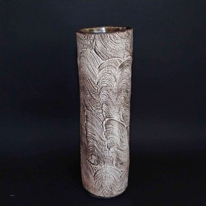 May include: A white ceramic vase with a brown, textured design. The vase has a cylindrical shape and a smooth, rounded rim.