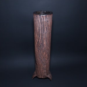 May include: A tall, brown ceramic vase with a wood grain pattern. The vase has a wide opening and a rounded base with three legs.
