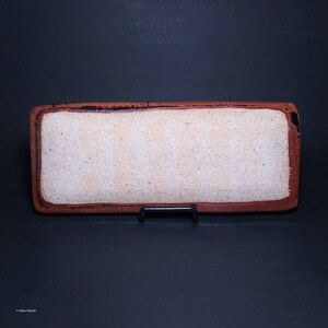 Puede incluir: Una bandeja rectangular de cer&aacute;mica con un interior blanco esmaltado y un borde marr&oacute;n rojizo. La bandeja est&aacute; sobre un soporte negro.