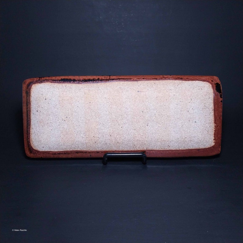 Puede incluir: Una bandeja rectangular de cer&aacute;mica con un interior blanco esmaltado y un borde marr&oacute;n rojizo. La bandeja est&aacute; sobre un soporte negro.