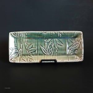 Puede incluir: Un plato rectangular de cerámica con un esmalte verde y un diseño en relieve de tallos y hojas de bambú.