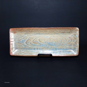 Op de afbeelding: Een rechthoekige serveerschaal van keramiek met een lichtblauw en bruin houtnerfpatroon. De schaal heeft een licht verhoogde rand en is geglazuurd met een glanzende afwerking.