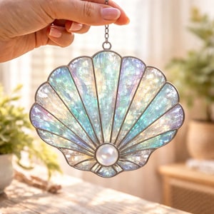 Pode incluir: Concha de vidro manchado iridescente com um centro de pérola, pendurada por uma corrente. A concha apresenta um design em forma de leque com tons de azul, verde e roxo. Uma peça decorativa para decoração costeira ou com tema de praia.