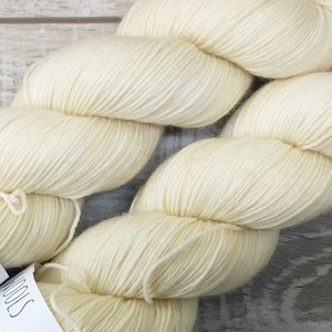 May include: Two skeins of cream-colored yarn labeled "Basic Sock" with the text "75% Superwash Merino, 25% Nylon, 100g, 400m, 437 yards" and "Blank Canvas" on the labels.