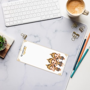 May include: A white notepad with the text "RUMDOUL Republic" and illustrations of three cartoon figures in traditional attire. The notepad is on a marble-patterned desk with a keyboard, pencils, and a cup of coffee.