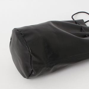 Puede incluir: Un bolso negro de cuero con cord&oacute;n y base redondeada. El bolso est&aacute; hecho de un material liso y brillante y tiene un cierre de cord&oacute;n en la parte superior. El bolso se muestra sobre un fondo blanco.