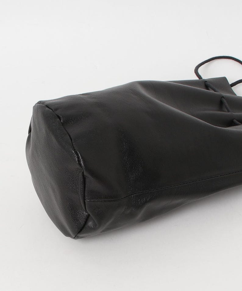 Puede incluir: Un bolso negro de cuero con cord&oacute;n y base redondeada. El bolso est&aacute; hecho de un material liso y brillante y tiene un cierre de cord&oacute;n en la parte superior. El bolso se muestra sobre un fondo blanco.