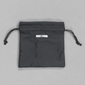 Puede incluir: Una bolsa negra con cord&oacute;n y una peque&ntilde;a etiqueta blanca. La bolsa est&aacute; hecha de una tela lisa y tiene forma rectangular. El cord&oacute;n es negro y est&aacute; anudado en ambos lados. La etiqueta tiene un peque&ntilde;o dise&ntilde;o estilizado.