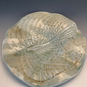 May include: A ceramic serving dish shaped like a large leaf with a light green glaze. The leaf has a detailed vein pattern and a slightly rippled surface.