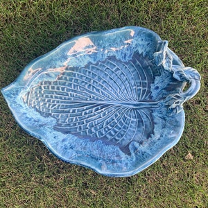 May include: A blue ceramic leaf-shaped serving dish with a raised design and a handle. The dish is glazed in a light blue color with a white glaze on the inside.