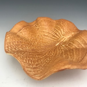 May include: A ceramic bowl with a wavy, leaf-shaped design. The bowl is a light brown color and has a textured surface.