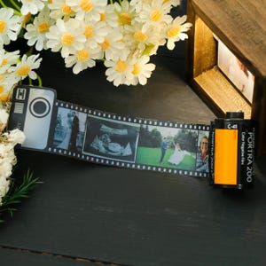 Pode incluir: Uma tira de filme decorativa com fotos de família, incluindo um casamento e uma ultrassonografia, ao lado de um rolo de filme Portra 200. Margaridas brancas e uma moldura de madeira no fundo. A tira de filme é em preto e branco.