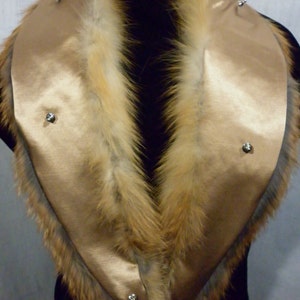 May include: A gold satin collar with a fox fur trim. The collar has four silver snaps on the front.