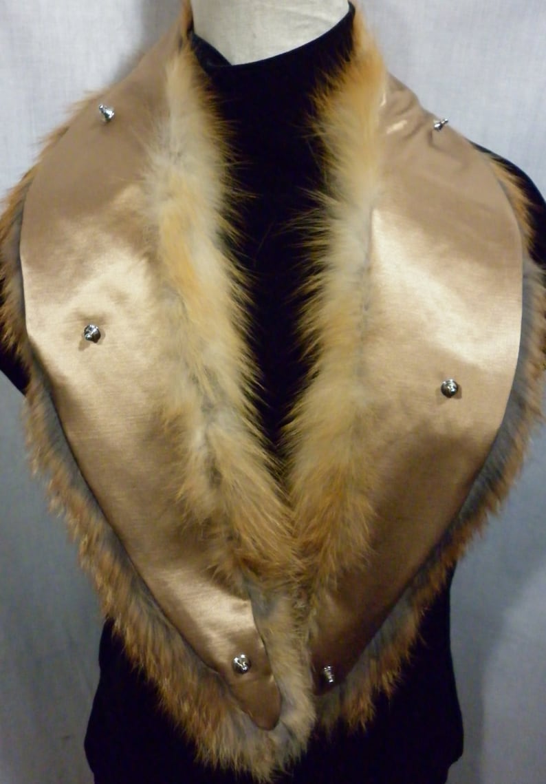 May include: A gold satin collar with a fox fur trim. The collar has four silver snaps on the front.