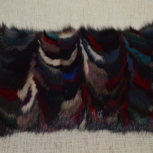 May include: A long rectangular pillow covered in a multi-colored faux fur fabric. The fur is a mix of black, brown, red, blue, and white. The pillow is soft and fluffy.