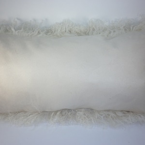 May include: A white rectangular pillow with a fluffy, white fur trim.