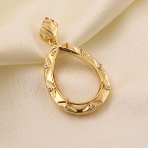 May include: A gold-toned teardrop-shaped pendant setting featuring a decorative leaf-like bail at the top. The frame is embellished with small, evenly spaced clear stones set into the metal, creating a polished and reflective surface finish.