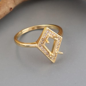 Puede incluir: Un anillo de tono dorado con un engaste en forma de cometa adornado con pequeñas piedras transparentes en pavé. El centro de la forma de cometa está abierto e incluye dos pequeñas garras metálicas diseñadas para sujetar una gema.