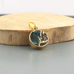 May include: A gold-colored pendant with a round, textured, teal and gold-colored stone. The pendant has a small loop at the top for a chain. The stone has a unique, natural pattern.