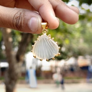 Pode incluir: Uma placa de madeira rústica branca com a palavra "Welcome" escrita à mão. A placa tem um aspeto envelhecido e um elemento floral decorativo. O fundo é uma textura de madeira desfocada.