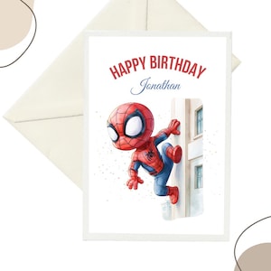 Könnte beinhalten: Eine rechteckige Grußkarte mit einer Cartoon-Illustration eines rot-blauen Superhelden, der eine Gebäudewand hochklettert. Der Text oben lautet Happy Birthday Jonathan in roter und blauer Schrift. Die Karte liegt vor einem weißen Umschlag.