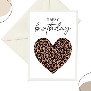 Könnte beinhalten: Eine weiße Geburtstagskarte mit einem Leopardenherz und den Worten "HAPPY birthday" in schwarzer Schrift. Ein cremefarbener Umschlag befindet sich hinter der Karte, mit abstrakten beigen Formen im Hintergrund.