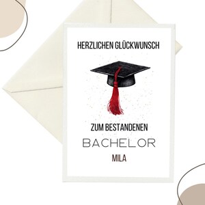Op de afbeelding: Een afstudeerkaart met een zwarte baret en een rode kwast illustratie. De kaart heeft de tekst "HERZLICHEN GLÜCKWUNSCH" bovenaan en "ZUM BESTANDENEN BACHELOR MILA" eronder. De kaart zit in een crème-kleurige envelop.
