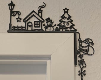 May include: A black L-shaped door corner decoration featuring a winter scene with a street lamp, a house, a snowman, and a Christmas tree on the top edge, and a figure of Santa Claus carrying a sack of gifts with snowflakes on the side edge.