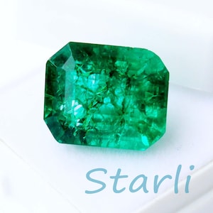 May include: A vibrant, emerald-cut green gemstone, set against a white background. The gem is rectangular with faceted edges, displaying internal textures. The word "Starli" is written in light blue script below the gem.