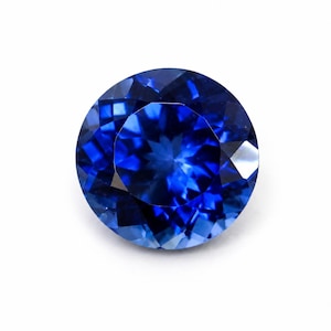 Könnte beinhalten: Ein runder, facettierter Saphir-Edelstein. Der Edelstein hat eine tiefe, lebendige blaue Farbe mit mehreren Facetten, die das Licht reflektieren. Der Edelstein ist vor einem weißen Hintergrund platziert.