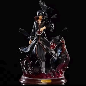 May include: A detailed figurine of a character in a long black coat with red accents, standing on a base with flames. The figure has black hair and is surrounded by dark crows. The base is brown with a gold-colored rectangular plate.