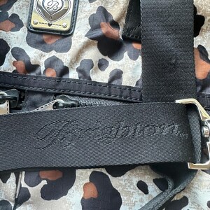 May include: A black and white leopard print bag with a black strap and a silver heart-shaped logo with the text "Juicy Couture" on the strap.