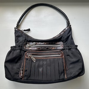 May include: A black nylon shoulder bag with brown leather accents and multiple pockets. The bag has a braided strap and a zipper closure.