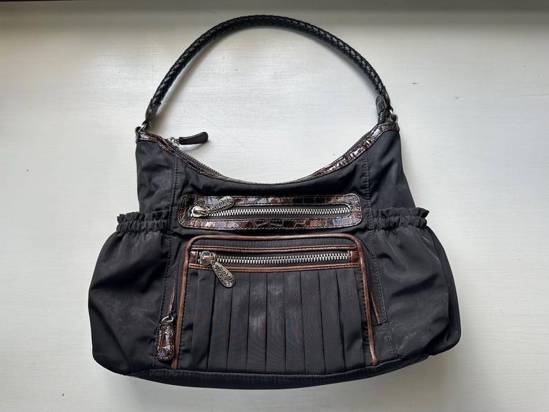 May include: A black nylon shoulder bag with brown leather accents and multiple pockets. The bag has a braided strap and a zipper closure.