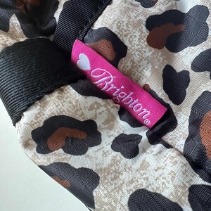 May include: A pink and white label with the word "Brighton" on it, attached to a beige and black leopard print fabric.