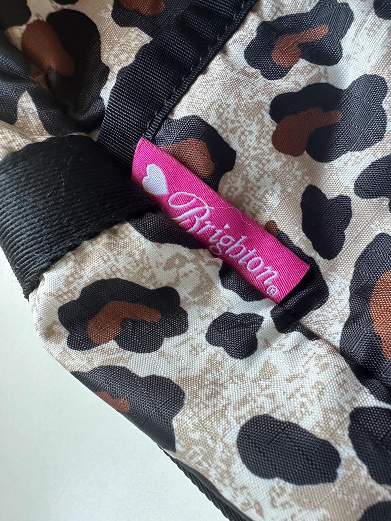 May include: A pink and white label with the word "Brighton" on it, attached to a beige and black leopard print fabric.