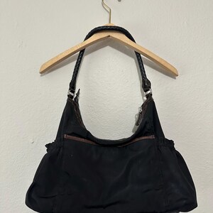 May include: A black nylon shoulder bag with brown leather accents and a braided strap.