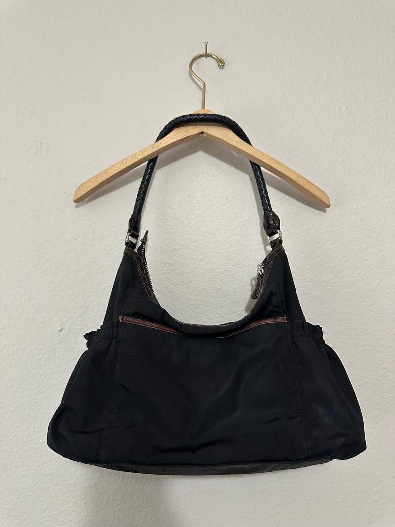 May include: A black nylon shoulder bag with brown leather accents and a braided strap.