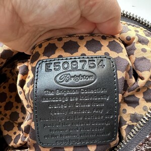 May include: Close-up of a black leather handbag tag with the text "The Brighton Collection handbags are individually crafted in China from quality leathers. Any markings on the surface are part of the natural beauty, texture and character of the leather, which makes each bag unique." and the number "E508754" above the text.