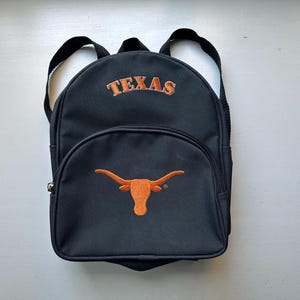 May include: Black backpack with a large orange embroidered Longhorn steer and the word "TEXAS" on the front.